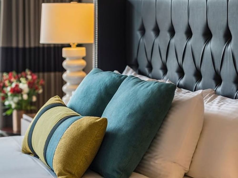 Teal and yellow pillows by a white lamp under a tufted black headboard in Emerald Suite at Warwick Seattle