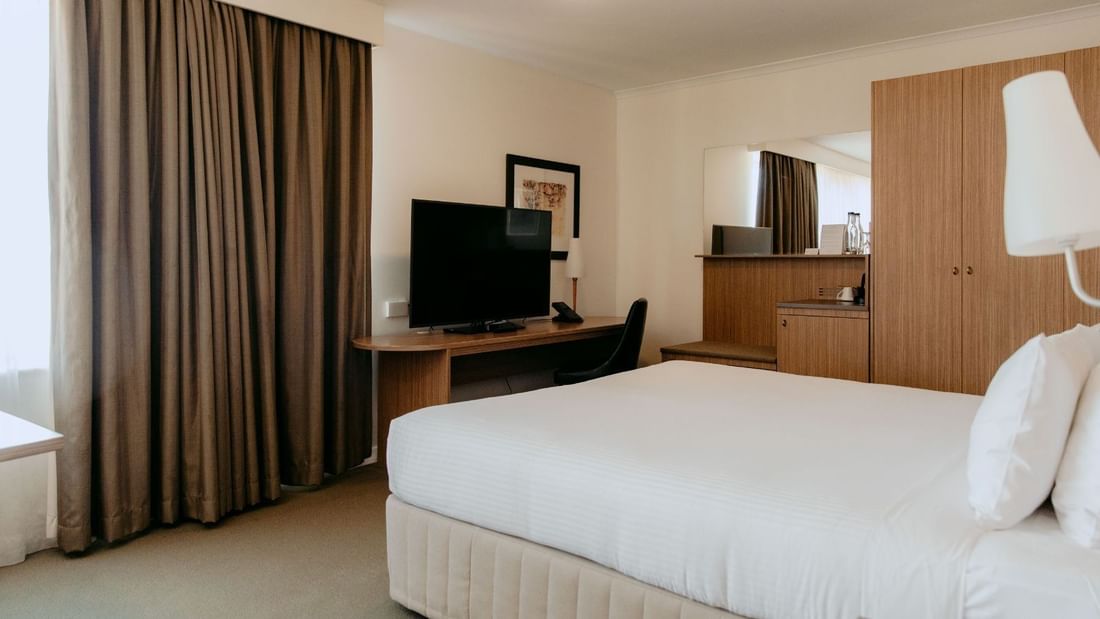 A hotel room with a large bed, desk, TV, and wooden cabinet with a mirror.