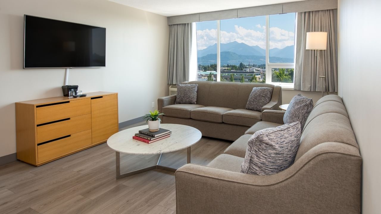 Hotel suite living area with two couches, coffee table, TV, and large window with mountain view.