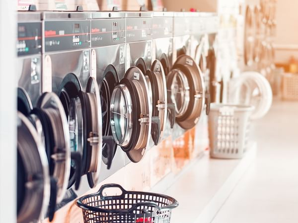Row of washing machines in a laundromat with baskets and a black basket on the floor.