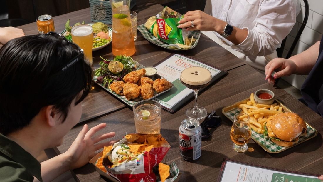 Guests enjoying pub food with burgers, nachos, and drinks at a table at The Brewery Bar + Kitchen Novotel Sydney Olympic