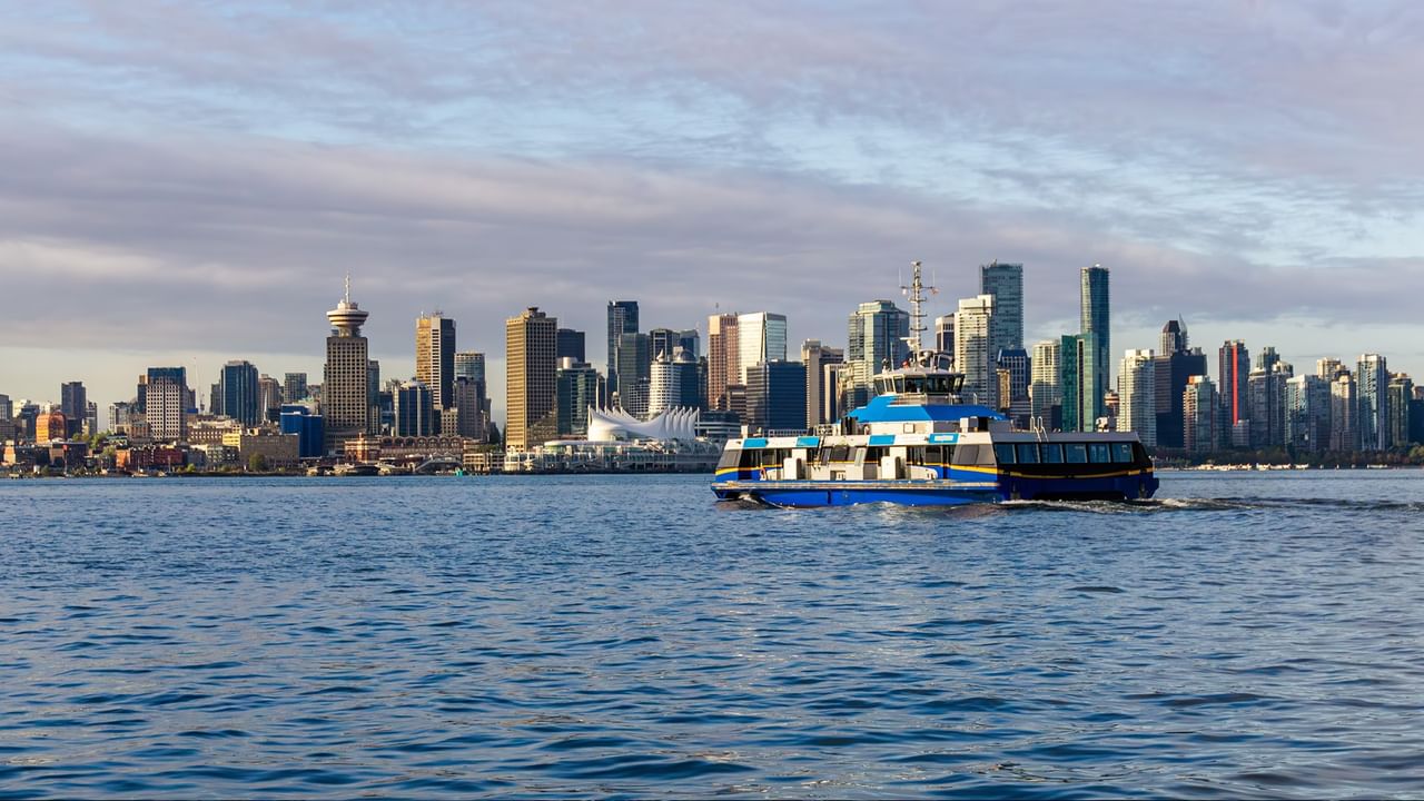Blue and white ferry boat traveling on water with a city skyline in the background.