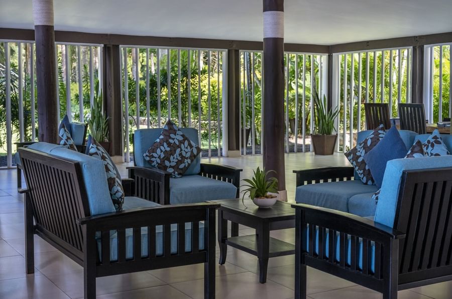 Blue armchairs with patterned pillows by a dark wood table under a white ceiling in the lobby at Tambua Sands Beach Resort