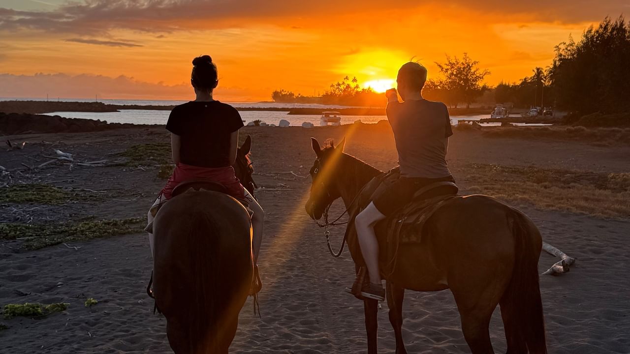 Two people riding horses on a beach at sunset.