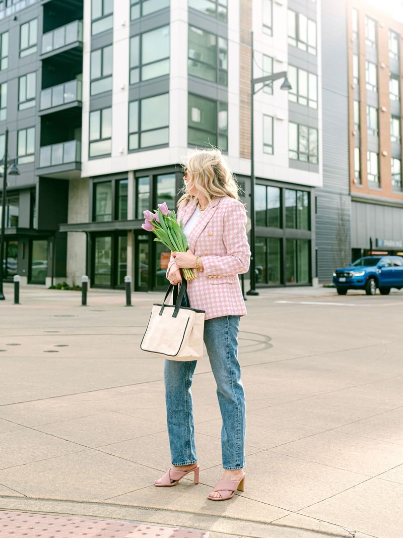 Woman in a pink blazer holding flowers and a tote bag by modern buildings near Warwick Seattle