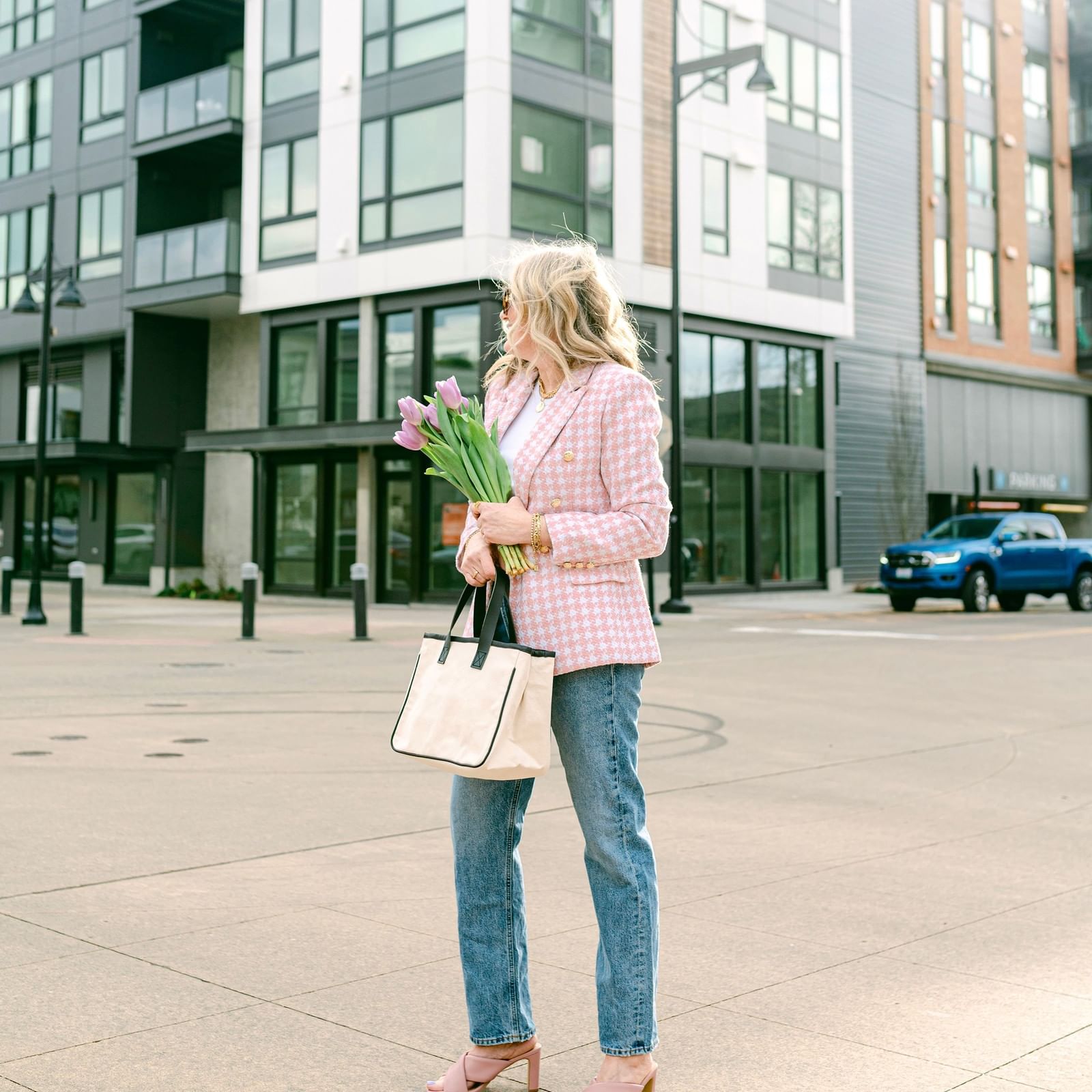 Woman in a pink blazer holding flowers and a tote bag by modern buildings near Warwick Seattle