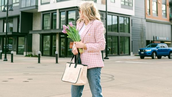 Woman in a pink blazer holding flowers and a tote bag by modern buildings near Warwick Seattle