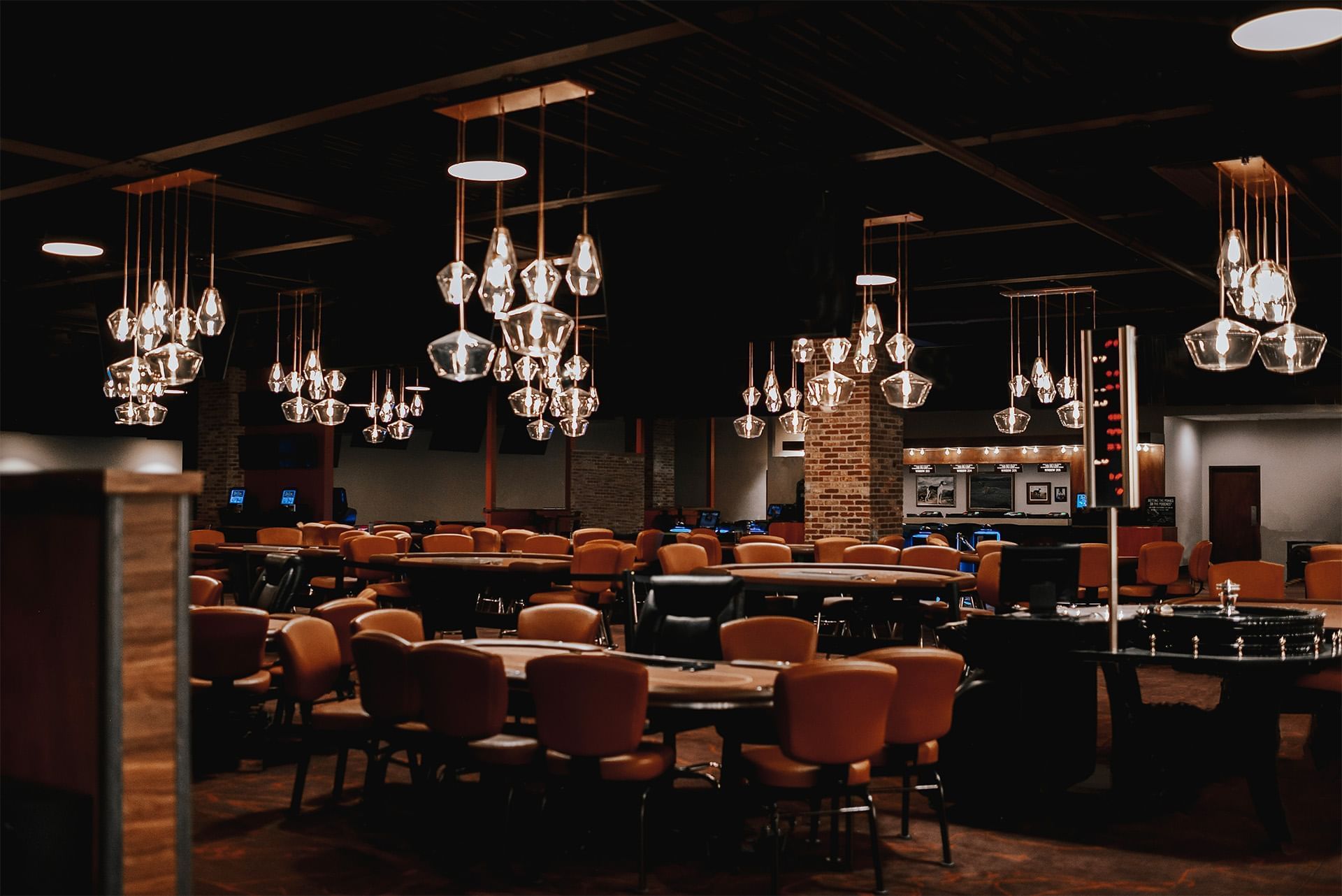 Casino gaming tables surrounded by leather chairs under glass pendant lights throughout the casino floor at The Brook
