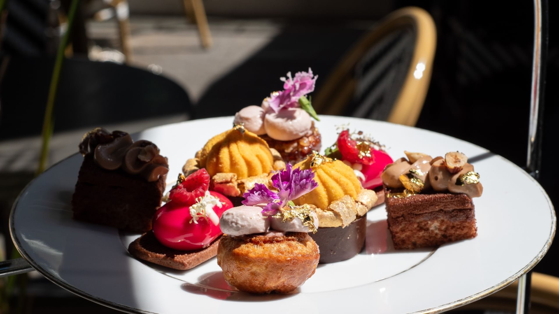 Assortment of various pastries, topped with edible flowers and gold leaf, on a white plate at Emporium Hotels Southbank