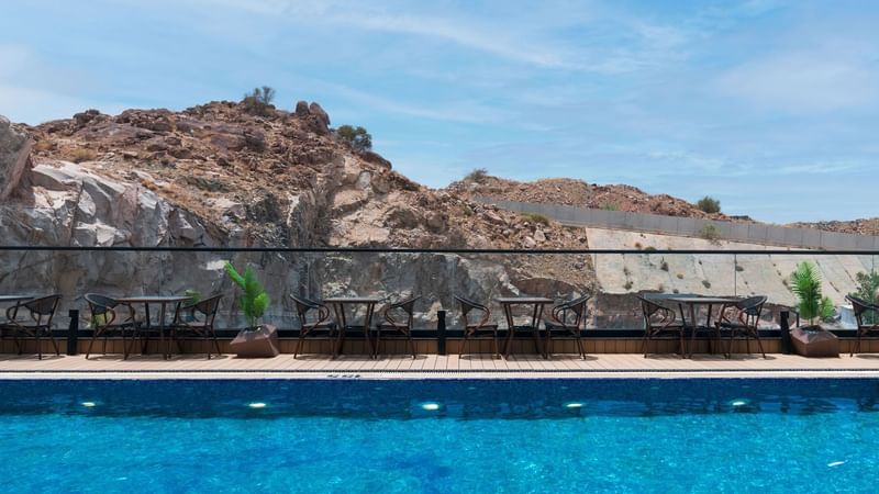 A serene poolside scene features a clear blue pool with wooden decking at Warwick Hotels and Resorts
