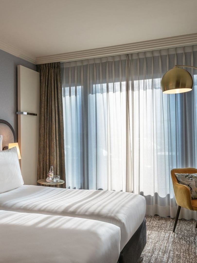 Classic Room with twin beds and a yellow armchair under an arc lamp by a large window at Warwick Geneva