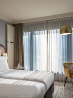 Classic Room with twin beds and a yellow armchair under an arc lamp by a large window at Warwick Geneva