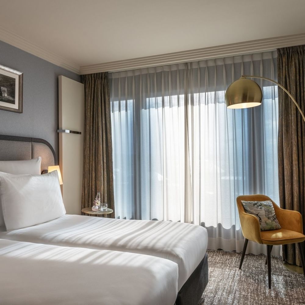 Classic Room with twin beds and a yellow armchair under an arc lamp by a large window at Warwick Geneva