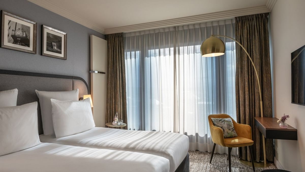 Classic Room with twin beds and a yellow armchair under an arc lamp by a large window at Warwick Geneva