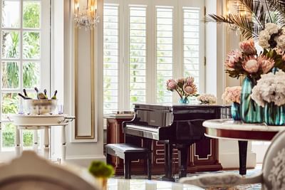 Park Lounge with a grand piano, floral arrangements, and a champagne display near shuttered windows at Park Hyatt Saigon