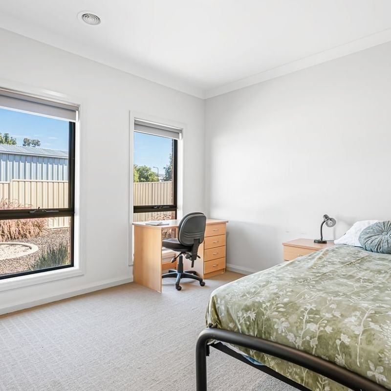 Room at La Trobe University Regional Housing with bed, desk, chair, and two windows.