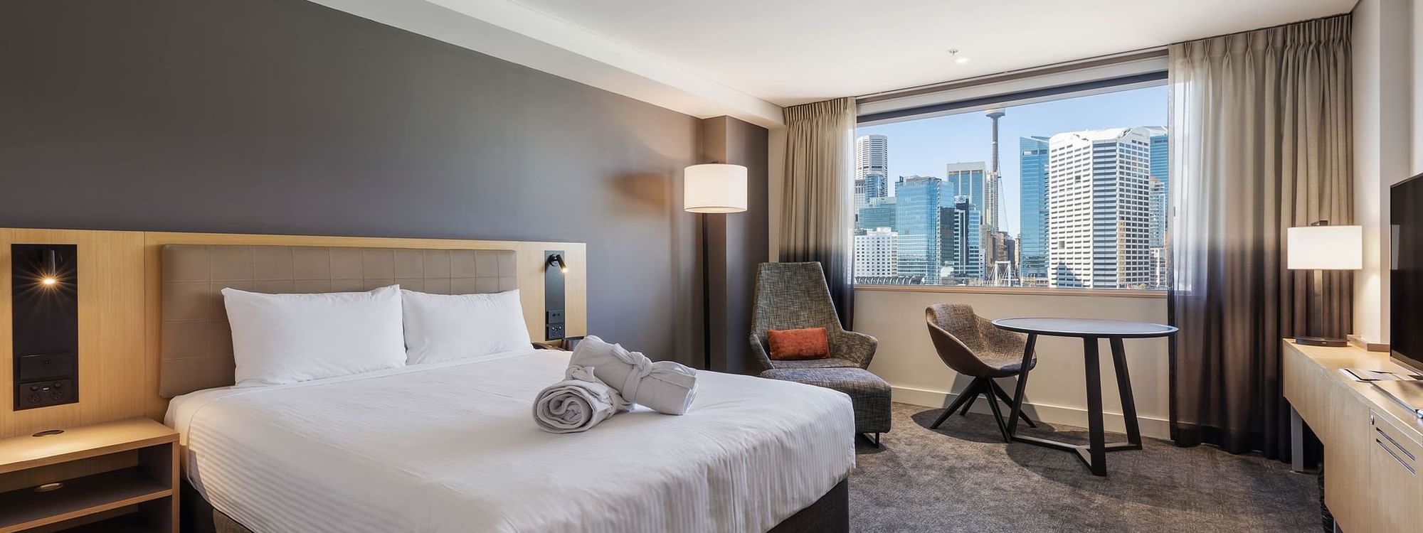 Seating area by the bed in Executive Queen Room with carpeted floors and a city view at Novotel Sydney on Darling Harbour