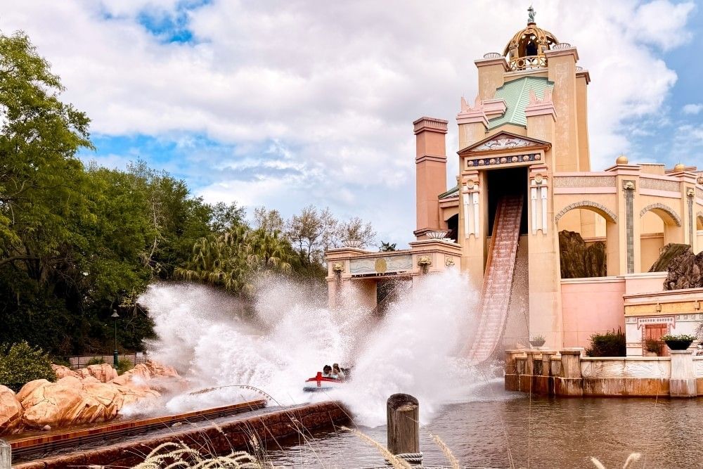 A small boat plunges into water with a big splash having just cascaded down a large drop hidden within a tall, palatial tower. 