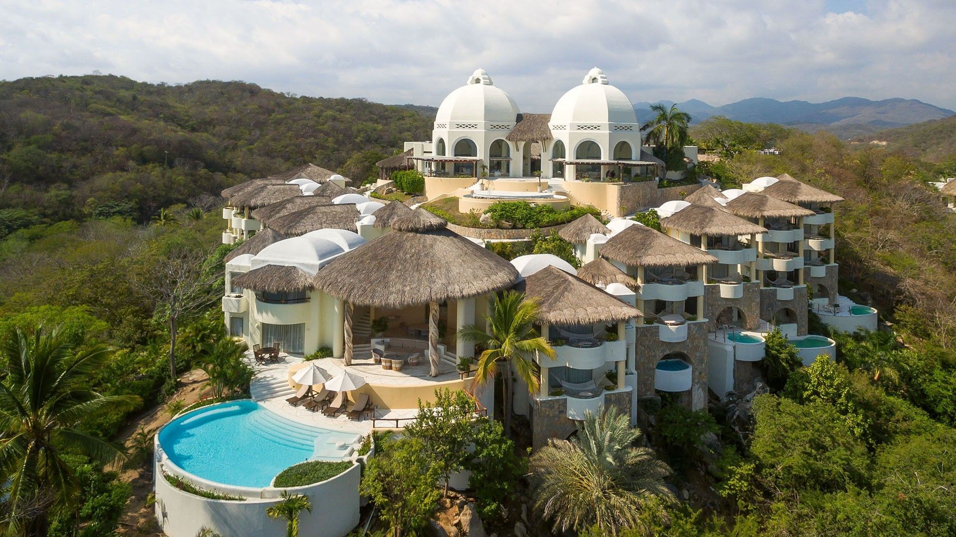 Aerial view of Quinta Real Huatulco featuring white domes by a pool surrounding thatched roofs