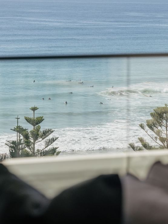 Coastal Two Bedroom Suite at Elysium Manly with an ocean view by pine trees under sheer curtains near a lounge chair