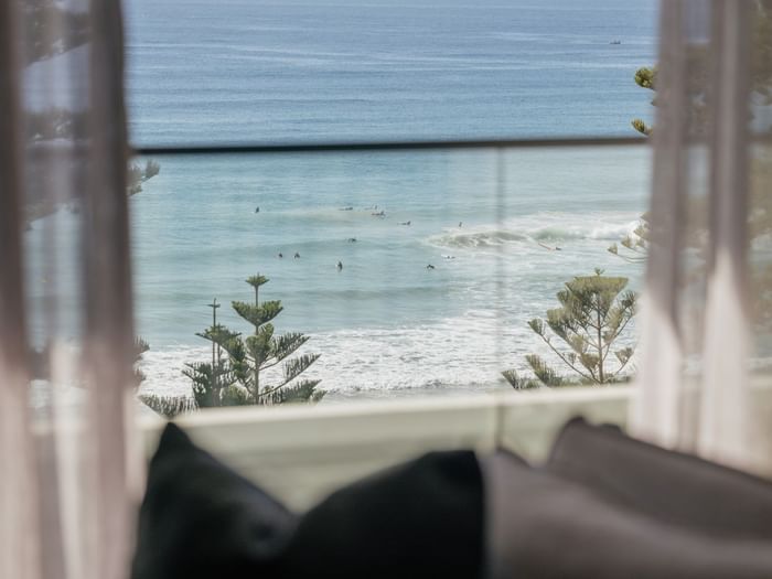 Coastal Two Bedroom Suite at Elysium Manly with an ocean view by pine trees under sheer curtains near a lounge chair