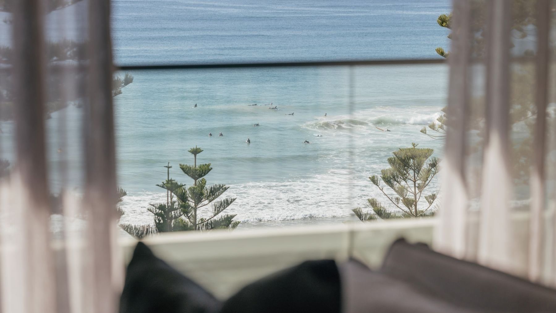Coastal Two Bedroom Suite at Elysium Manly with an ocean view by pine trees under sheer curtains near a lounge chair