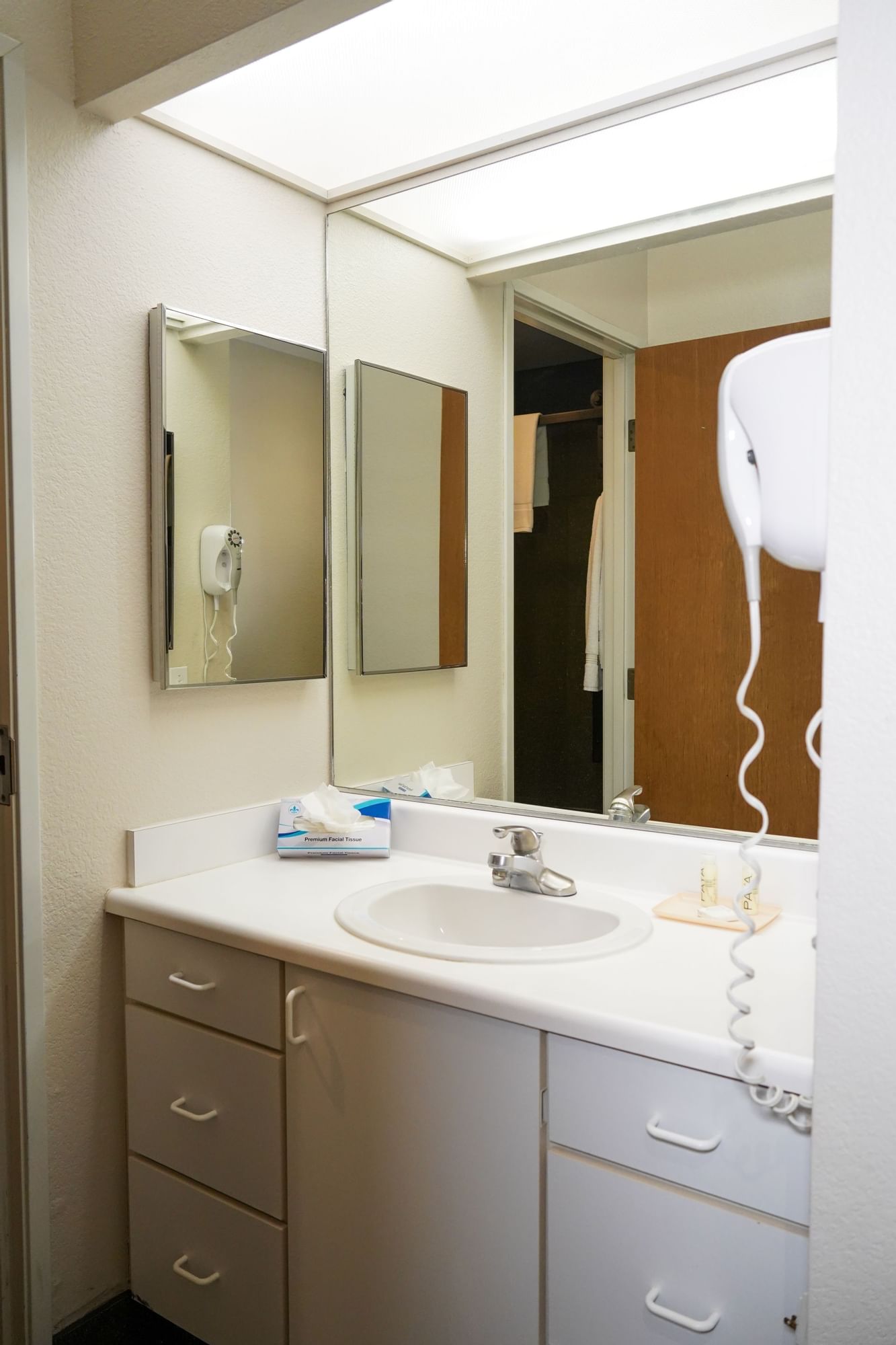 A bathroom sink area with a white sink, mirror, tissue box, and hair dryer.