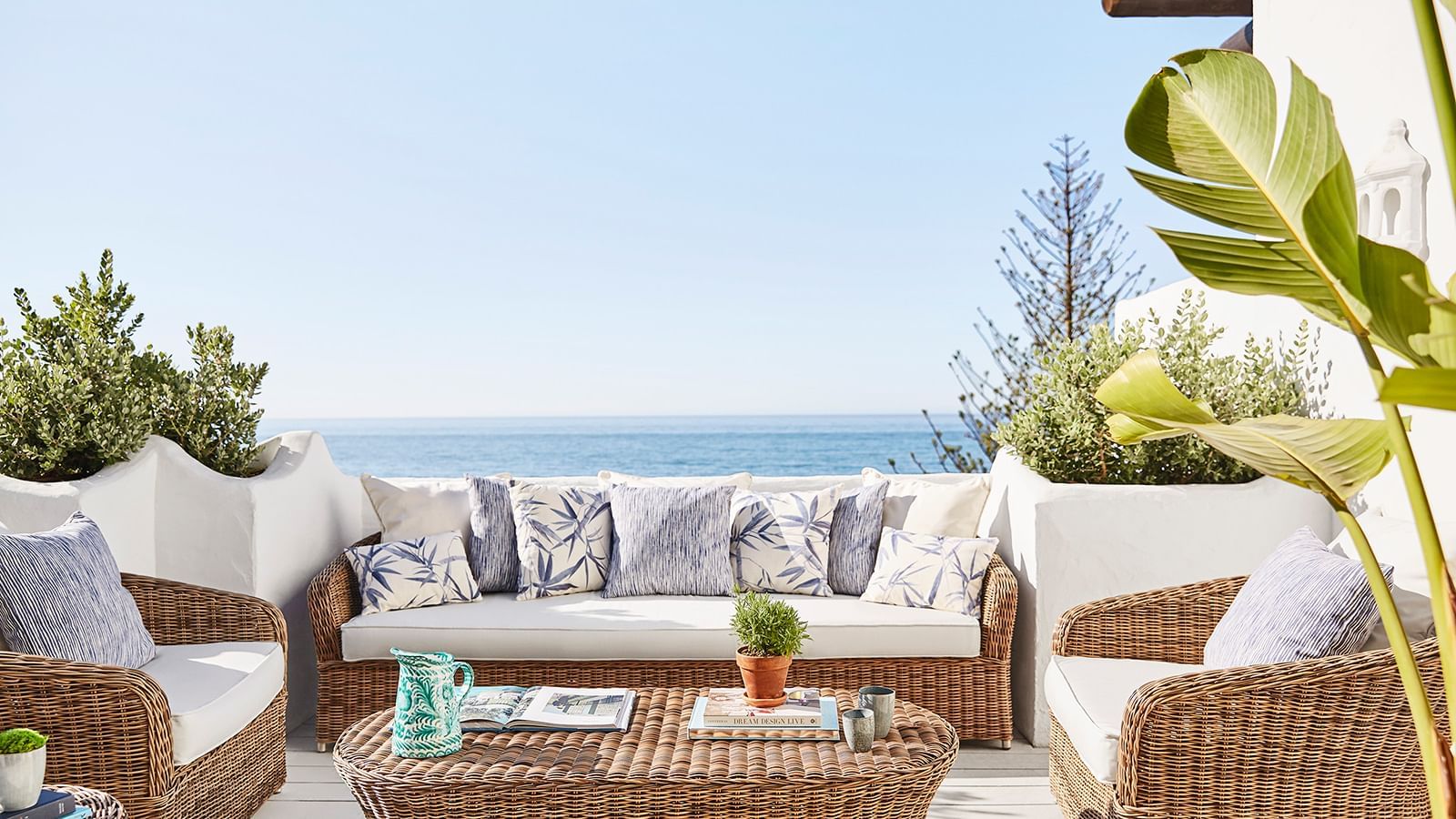 Rattan sofa and chairs with blue and white pillows placed on a deck near the ocean at the Marbella Club