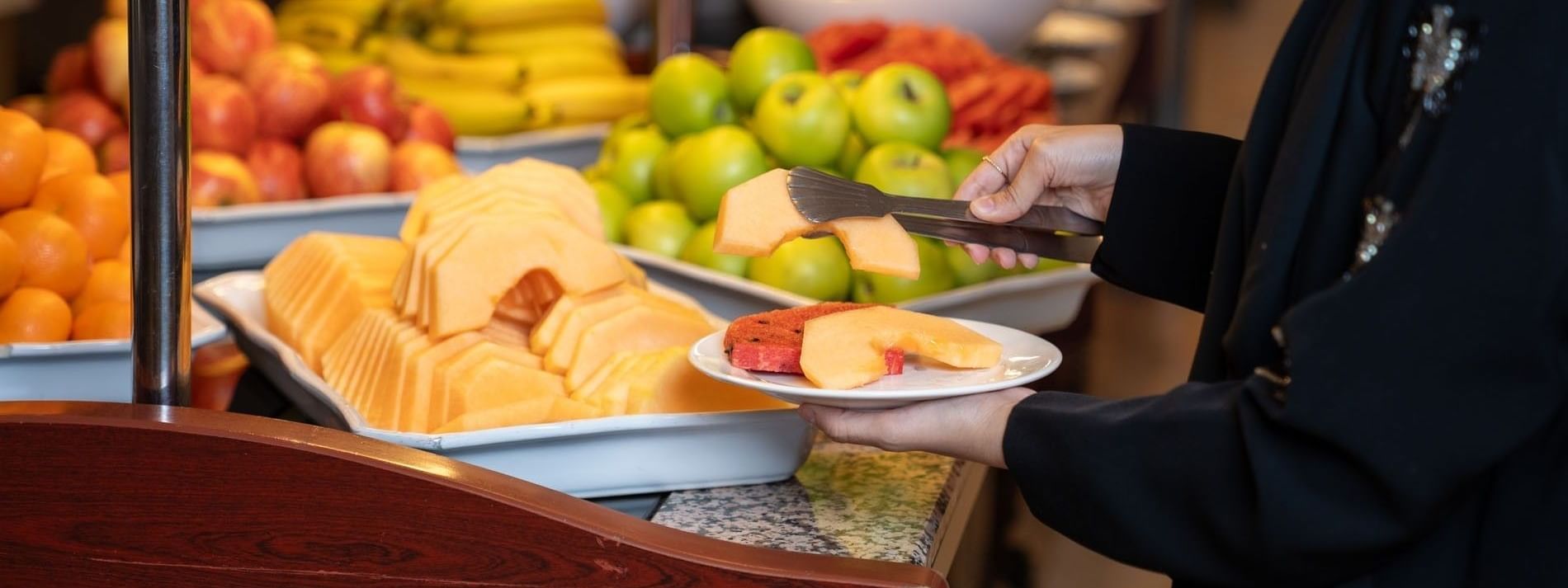 Person serve fresh sliced melon onto  white plate at breakfast buffet at Saja Warwick Madinah
