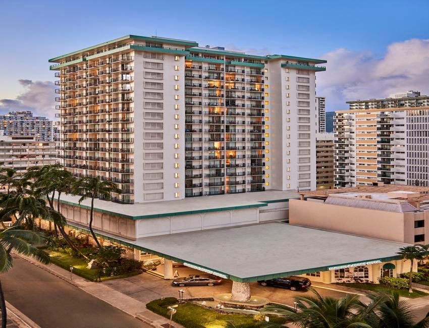 A high-rise building with balconies and a parking garage in front of it.
