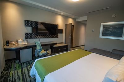 Neat double bed with a green throw runner placed by an office desk under a flat-screen TV in Superior Room at Hotel Mirra
