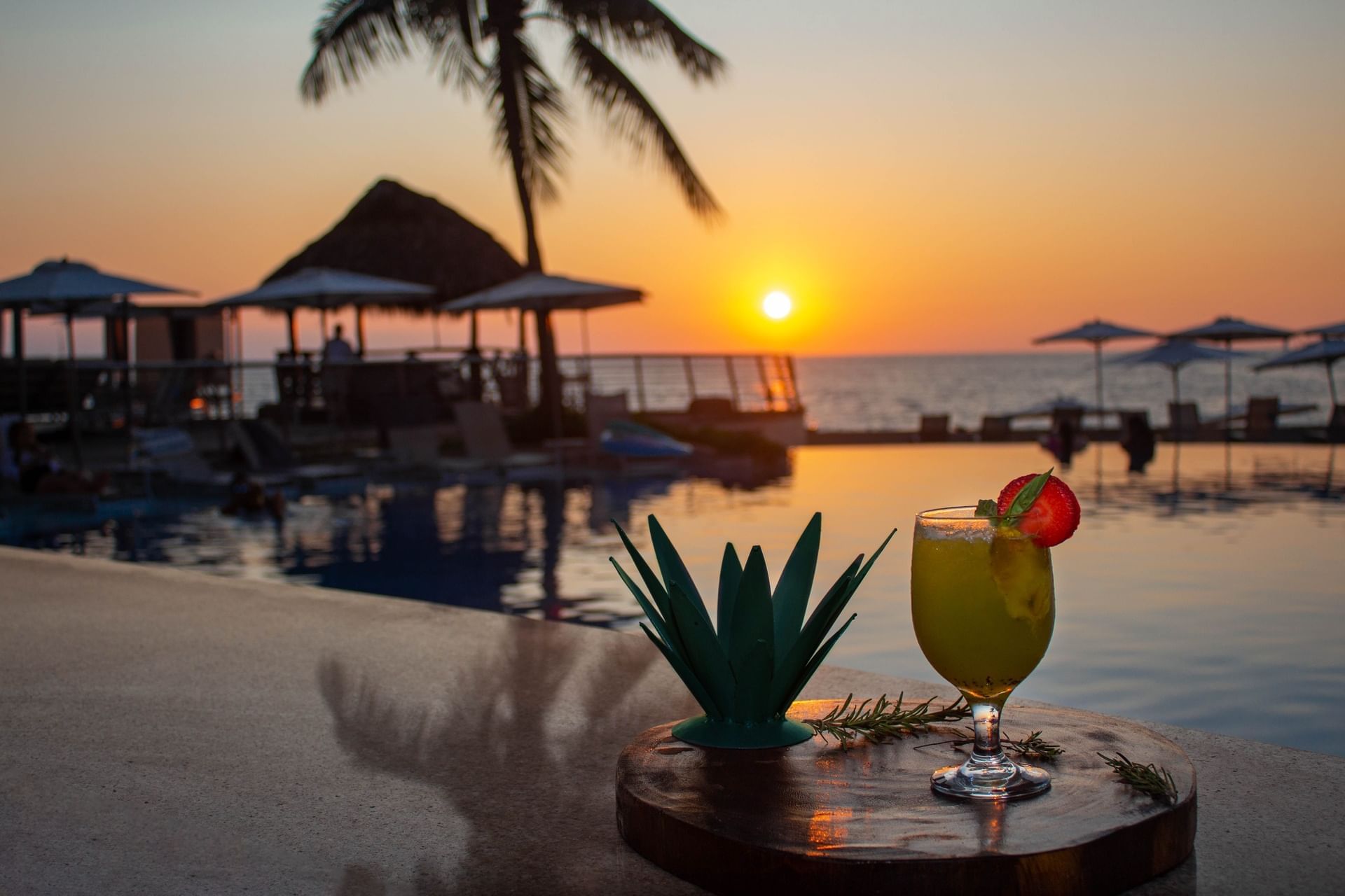 Cocktail on a wooden table, with a sunset over a pool and palm trees at Sunset Plaza Beach Resort, Sunset Plaza hotel