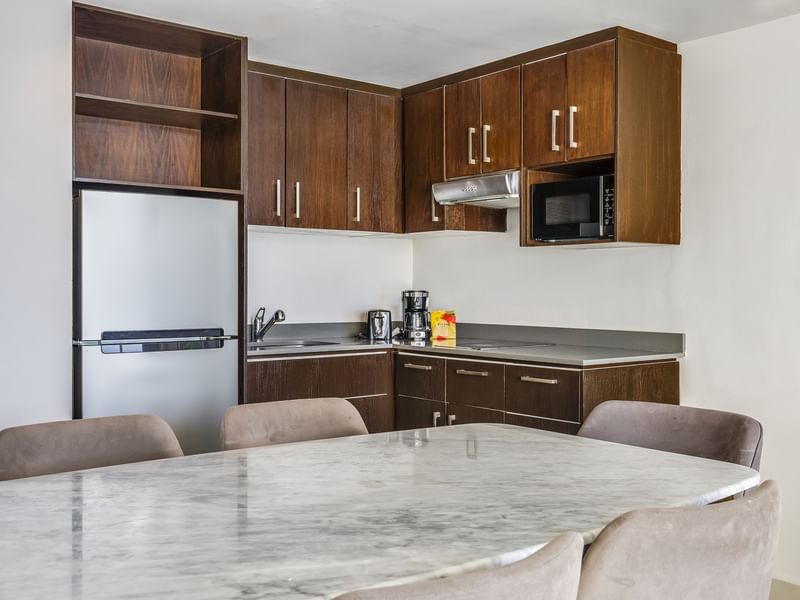 Luxury Suite kitchenette with dark wood cabinets, a silver fridge, and a marble-glazed table at Sunvivia Mazatlán
