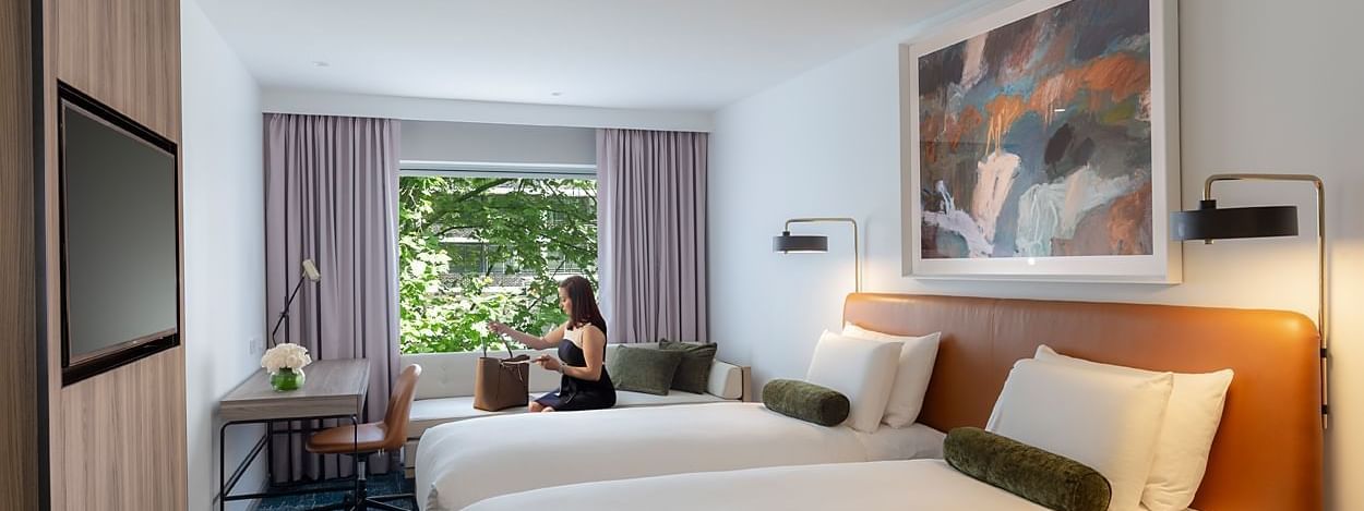 Woman with handbag sitting on window bench near two twin beds in Superior Twin Room at Novotel Sydney Darling Square