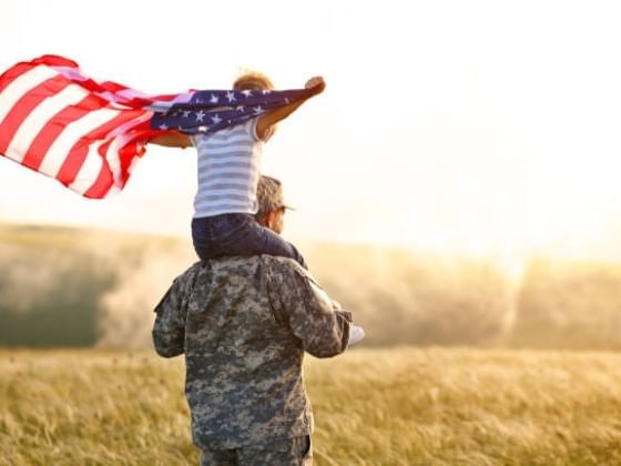 Child holding a flag while sitting on the shoulders of a military family member.