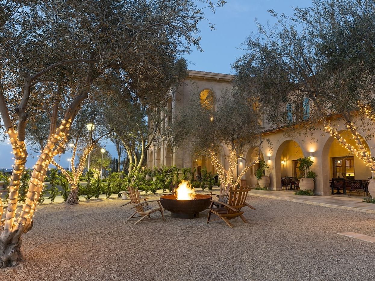 The front courtyard fire pit lit with four wooden chairs in the evening 