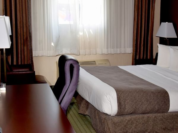 Hotel room with a bed, desk, chair, and window with curtains.