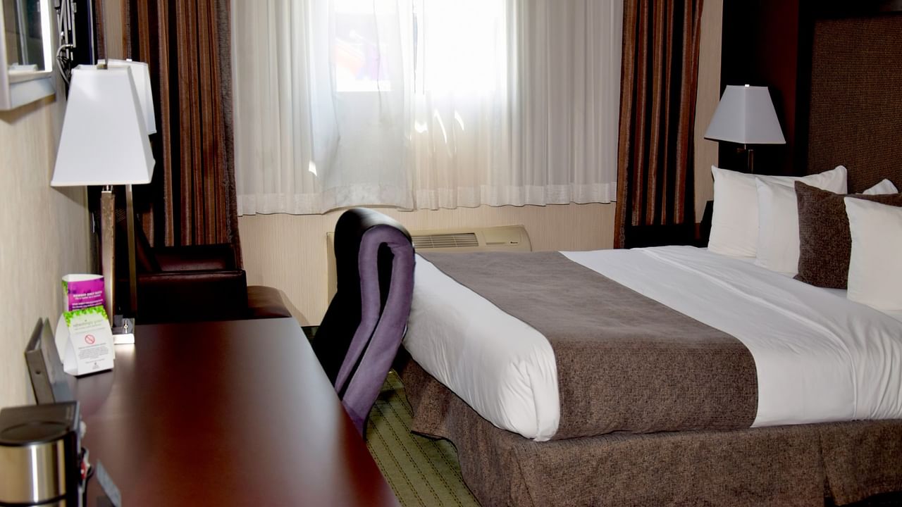 Hotel room with a bed, desk, chair, and window with curtains.