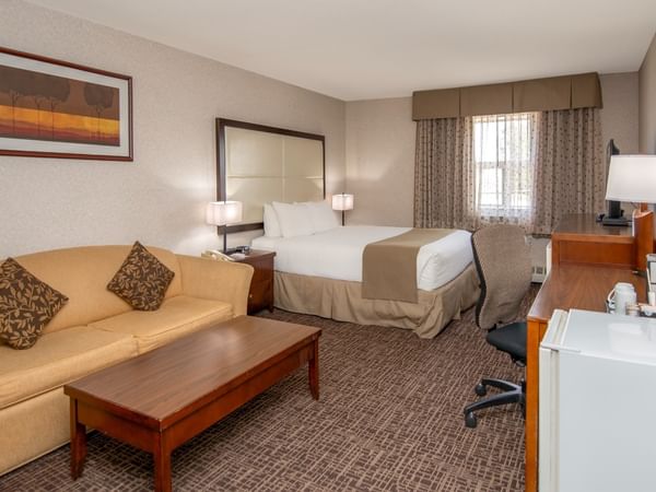 Hotel room with couch, coffee table, bed, desk, chair, and framed artwork on the wall.