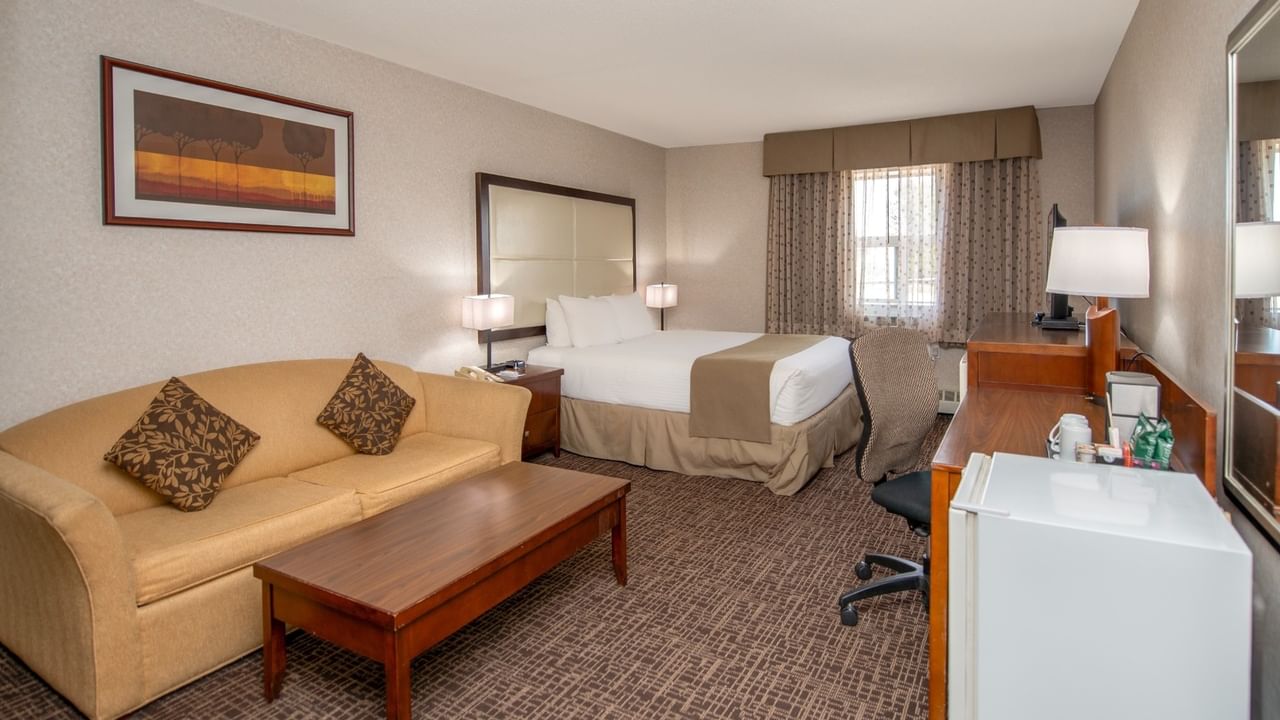 Hotel room with couch, coffee table, bed, desk, chair, and framed artwork on the wall.