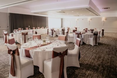 Ballroom wedding at The Aberdeen Altens Hotel with round tables and chairs decorated with brown ribbons