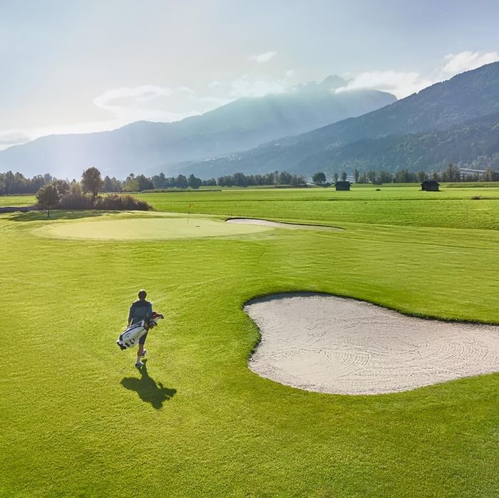 Golfer walking on a lush green course with a sand bunker near Falkensteiner Hotel and Spa Carinzia