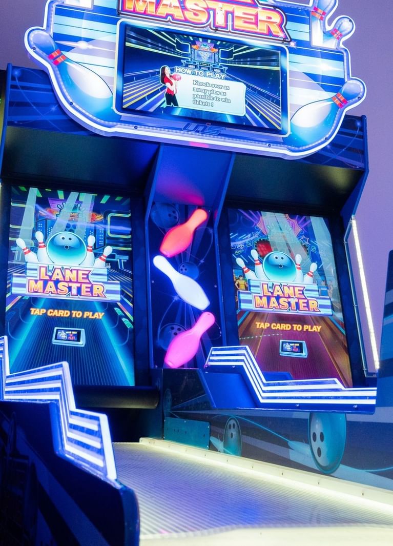 Lane Master bowling arcade with glowing pins between two screens, beside a ball return ramp at Hotel X Toronto