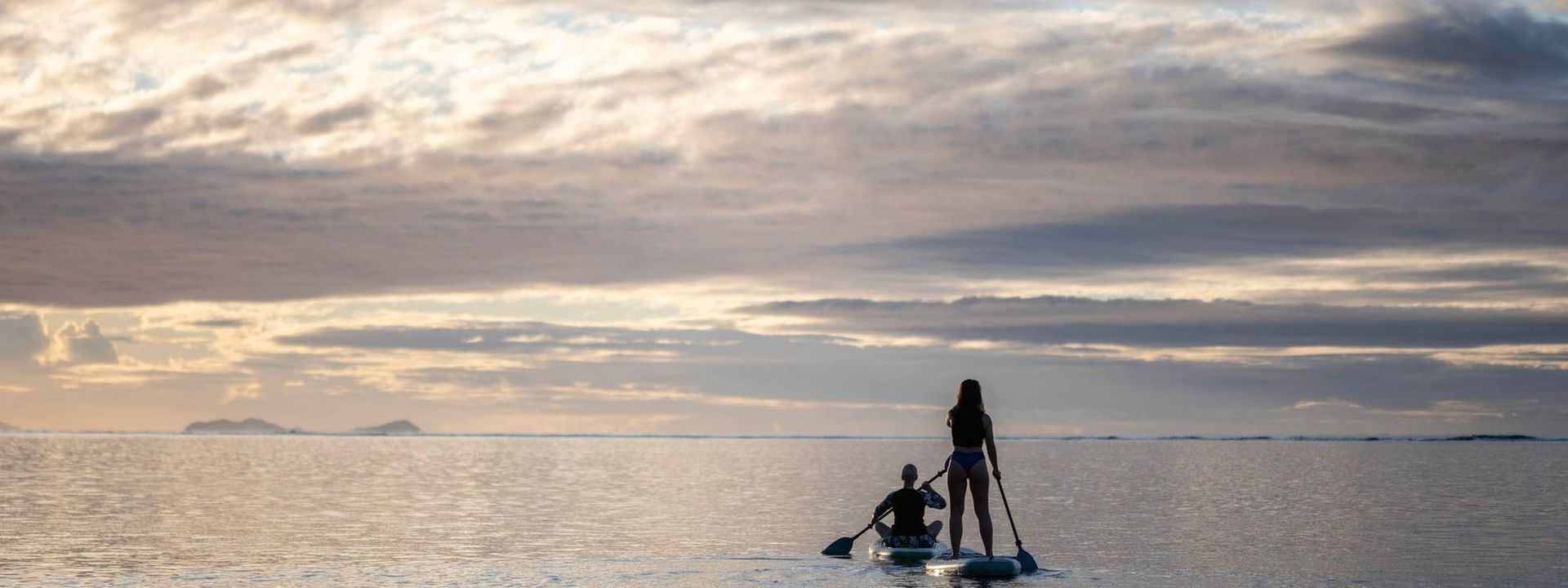 Two guests on paddleboards by calm waves under a golden evening sky at Warwick Fiji Resort and Spa in Korolevu