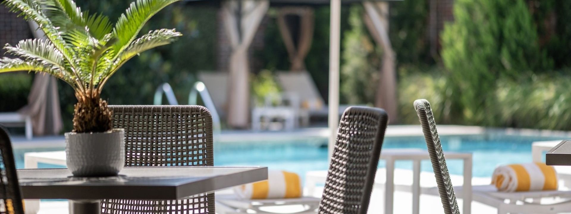 Woven chairs by a table under a white umbrella surrounding the pool deck area at Warwick Melrose Dallas