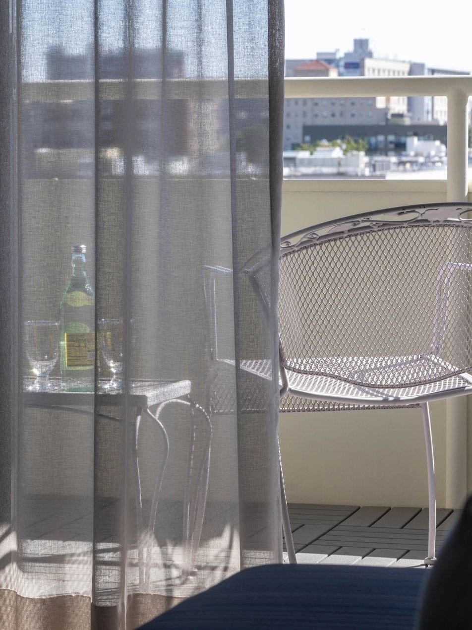 Balcony chairs by a table with water under a sunny sky through sheer curtains in Deluxe Rooms at Warwick Denver