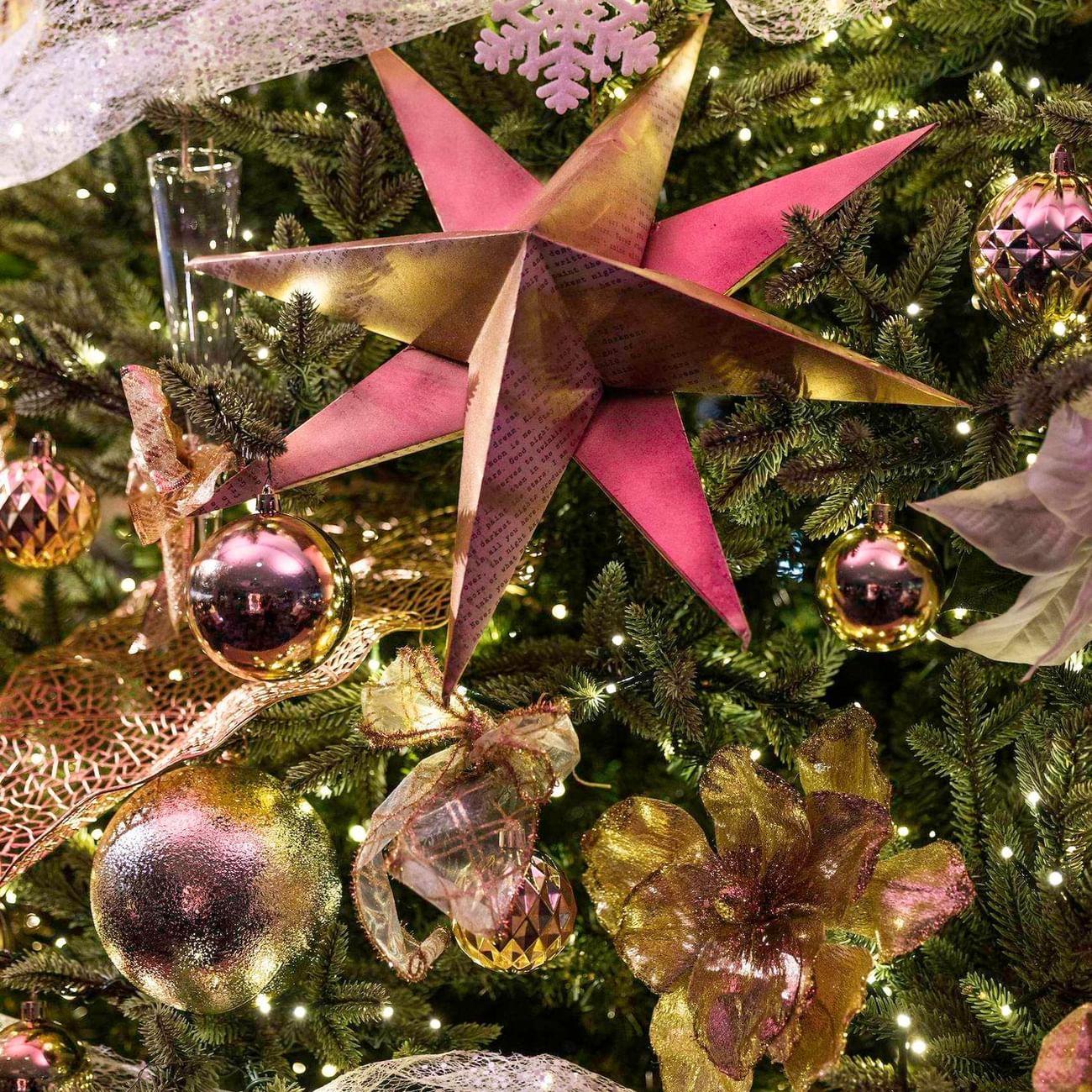 Decorated Christmas tree with gold, pink, and white ornaments, ribbons, and twinkling lights in festive display