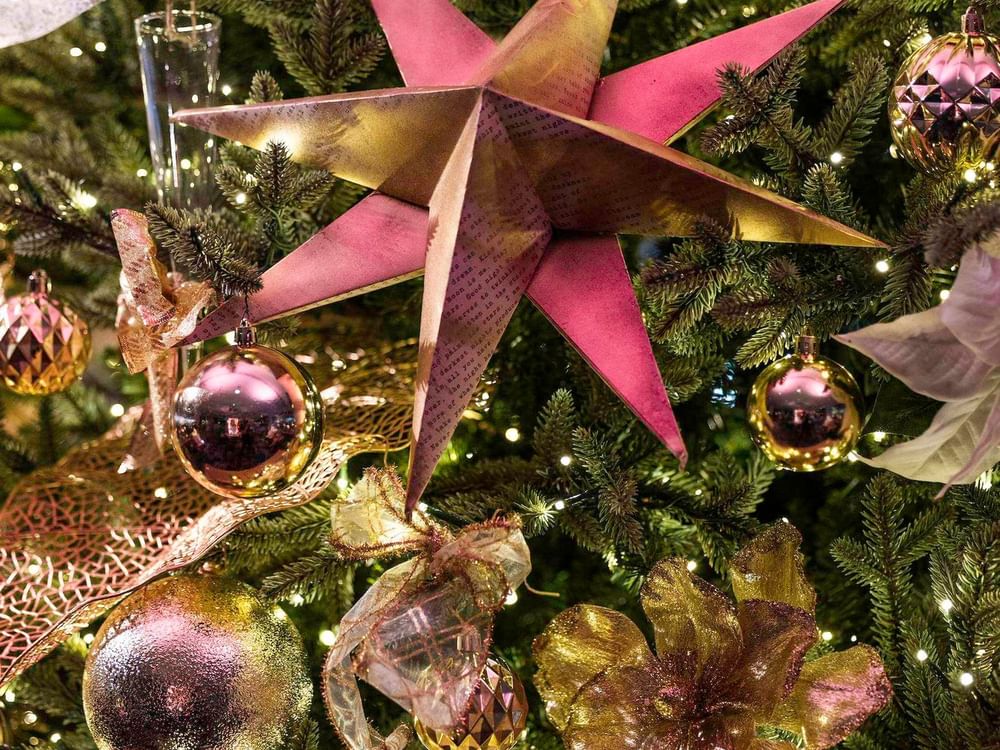 Decorated Christmas tree with gold, pink, and white ornaments, ribbons, and twinkling lights in festive display