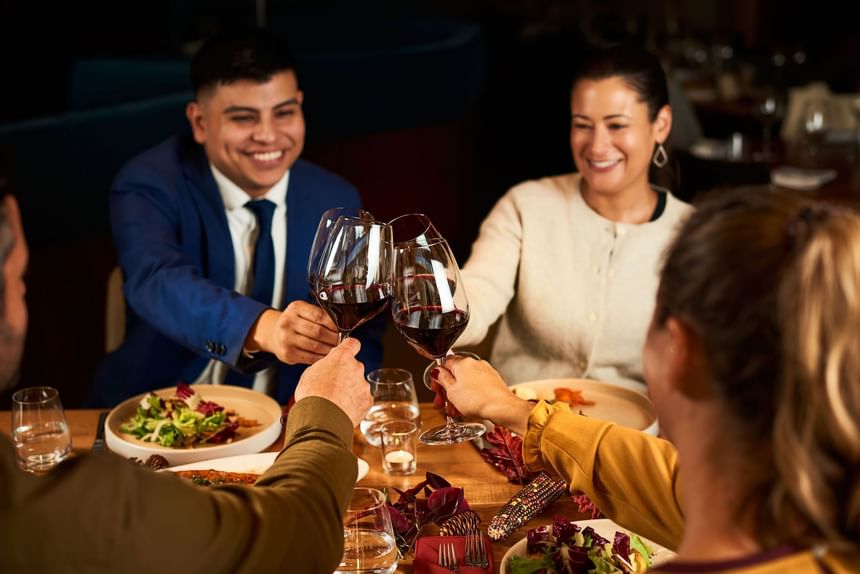 Three people toasting with wine glasses at a dining table filled with food at the Hotel Arista.