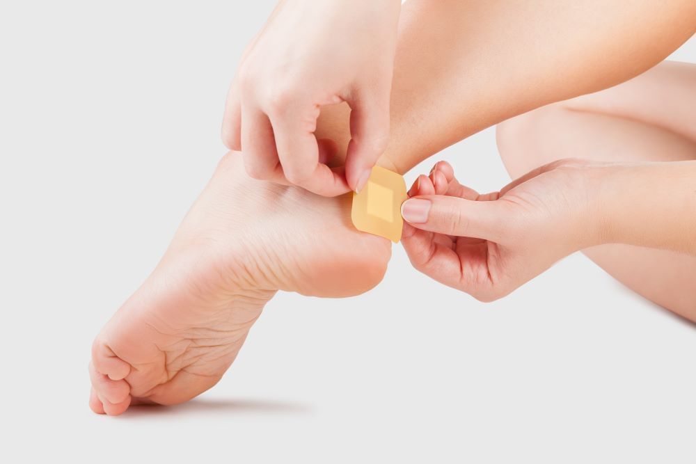 A person places a small square bandage on their heel. 